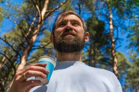 Man drinking refreshing beverage from paper cup outdoors in summer forest Stock-Fotos