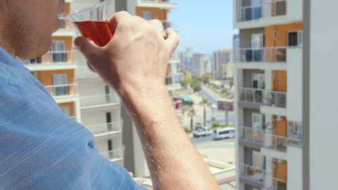 Man drinking tea from a glass cup standing on the balcony of his apartment 스톡 동영상 263095781