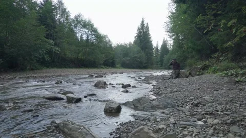 Man drinking tea on the riverbank during a light rain, hiking Stock Footage 211816086