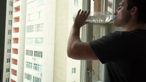 Man drinking water from a bottle standing by the window defocus Video stock 162038903