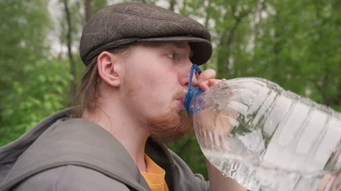 Man Drinking Water from Large Plastic Bottle in Park with Trees and Background Stock Footage 345085127