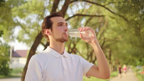 Man drinking water from a plastic bottle outdoors. Young adult drinking cle.. Vídeo Stock 339535011