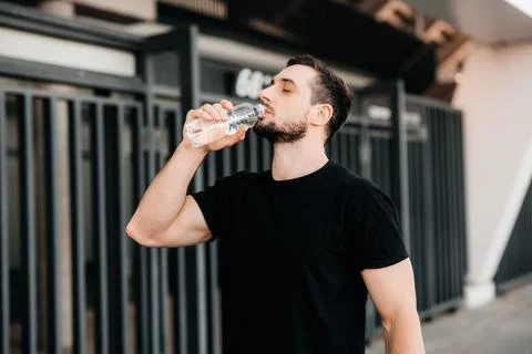 Man drinking water from plastic bottle after jogging with closed eyes. Hard Stock Photos