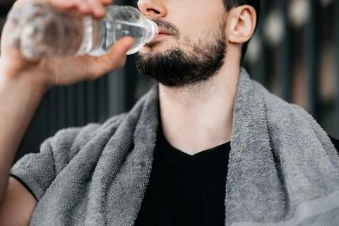 Man drinking water from plastic bottle after hard workout. Close up cut view of Stock Photos