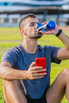 Man drinking water while holding smartphone outdoors in park.Vertical Stock Photos