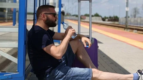 Man drinking water while sitting on the platform and waiting for his train Stock Footage 78654052