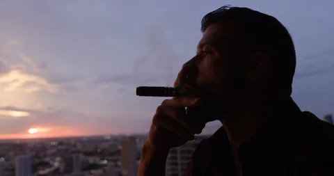 Man drinking whisky while smoking cigar at dusk Stock Footage 116350024
