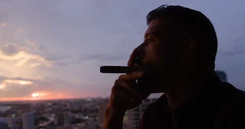 Man drinking whisky while smoking cigar at dusk Stock Footage 116350504