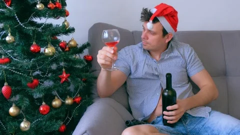 Man is drinking wine from bottle and glass sitting on couch near Christmas tree. Stock Footage 136520473