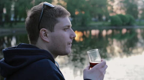 Man drinking wine sitting near the lake in the park Stock Footage 64488434