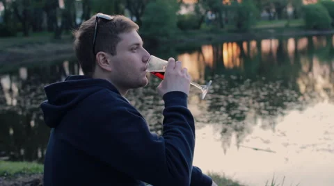 Man drinking wine sitting near the lake in the park Stock-Footage 64488951
