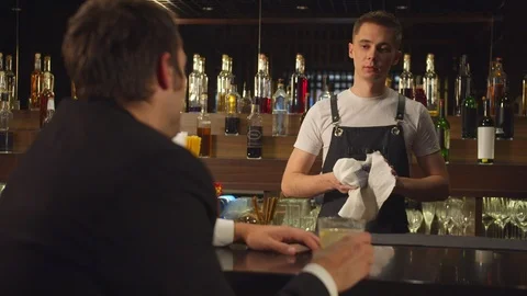 Man drinks alcohol and talks to bartender who wipes a glass Stock Footage 123687251