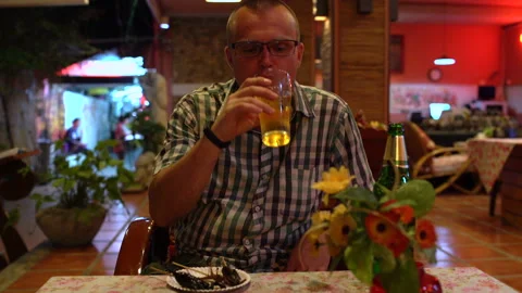 A man drinks beer and eats a roasted grasshopper in a Thai restaurant Stock Footage 91820483