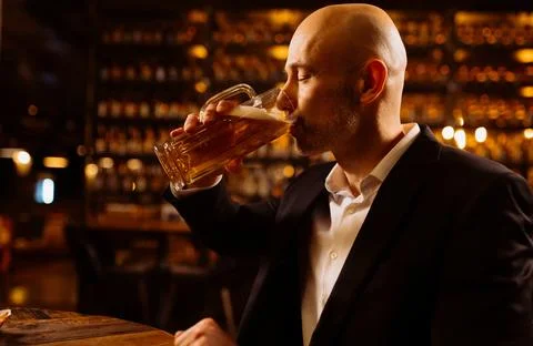 A man drinks beer. Side view of handsome bald man drinking beer in pub Foto stock