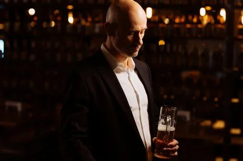 A man drinks beer. Side view of handsome bald man drinking beer in evening pu Stock Photos