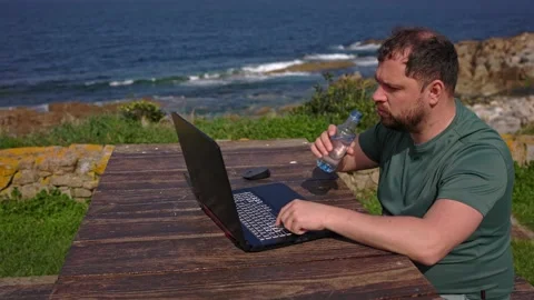 A man drinks a cart while working at a computer in nature. Stock Footage 189916755