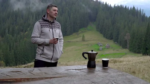 A man drinks coffee and looks at the beautiful landscape. Coffee maker and mug Stock Footage 142157243