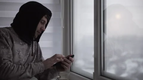 A man drinks coffee and uses a smartphone while sitting alone on a balcony  Stock Footage 146657819