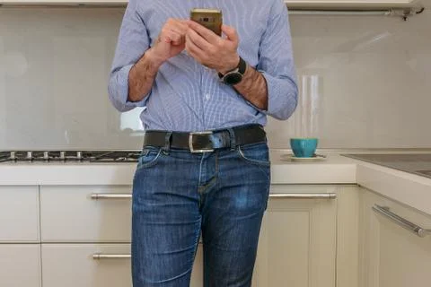 Man drinks a coffee in the kitchen and in the meantime looks at the smartphon Stock Photos