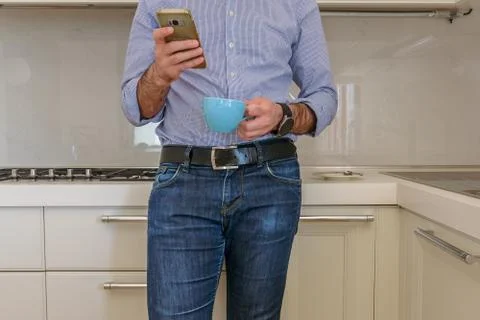 Man drinks a coffee in the kitchen and in the meantime looks at the smartphon Stock Photos
