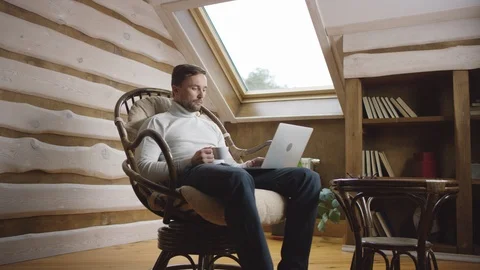 Man drinks coffee by laptop on the attic Stock Footage 100345269