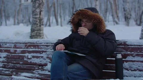 A man drinks coffee from a mug and uses a tablet while sitting on a bench Stock Footage 179996437