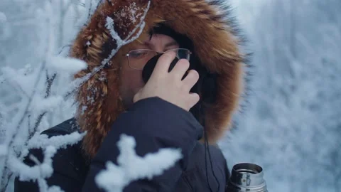 A man drinks coffee from a mug next to snow-covered branches Stock Footage 179997737
