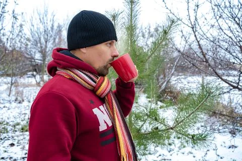 A man drinks coffee or tea outside on a frosty day. Snow all around Stock Photos