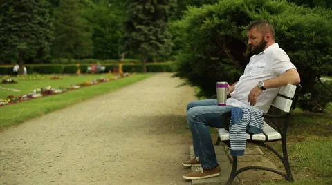 Man drinks coffee, sitting on a bench at the park Stock Footage 64283153