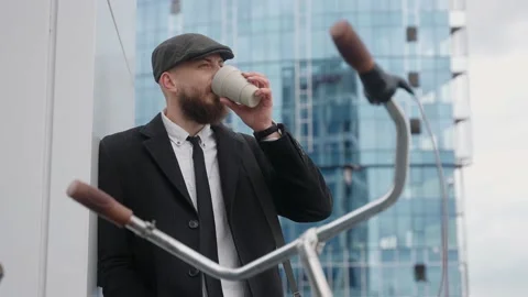 A man drinks coffee in a suit and hat near a business center Video stock 199394797