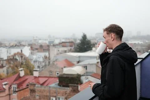 A man drinks coffee on a terrace while holding a cigarette and looking over the Fotos Stock