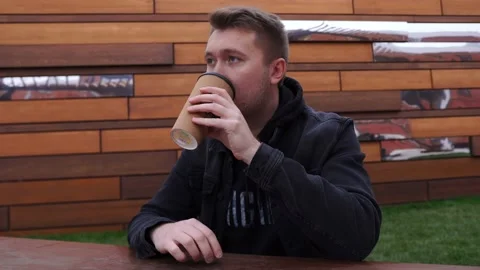 Man drinks coffee from thermo mug on the street, drum his fingers on the table Stock Footage 141785982