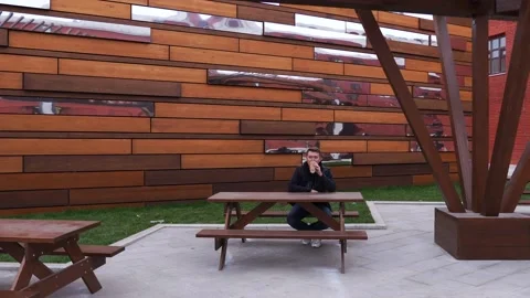 Man drinks coffee from a thermo mug in an urban environment at table on a bench Stock Footage 141786022