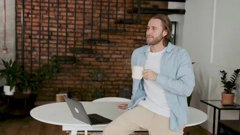 Man drinks coffee at the workplace and looks at the camera. In a stylish office Video stock 196010332