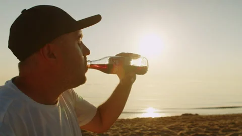 Man drinks a cold bottle of Coca Cola while sitting on the beach Video stock 205704697