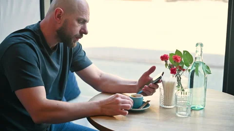 Man drinks espresso while checking smartphone at cafe table Stock Footage 346725442