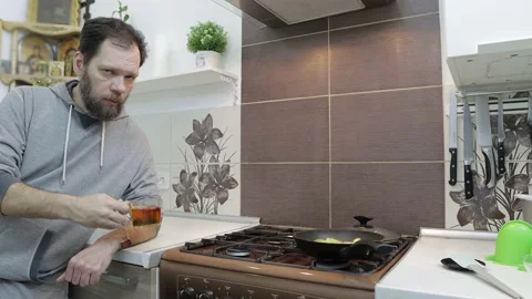 A man drinks herbal tea with berries at home in the kitchen and looks directly 動画素材 169700163