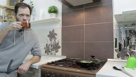 A man drinks herbal tea with berries at home in the kitchen and looks directly Stock Footage 205465136
