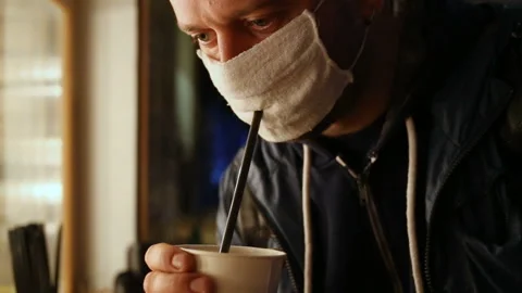A man drinks hot coffee from a disposable Cup through a hole in the mask. Rea Stock Footage 131093456