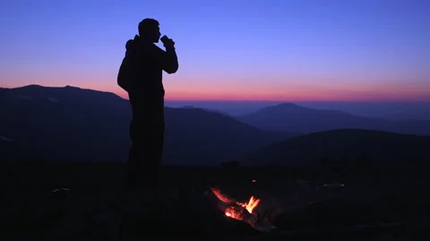 A man drinks a hot drink at night by a campfire in a tourist camp  Stock Footage 135898859