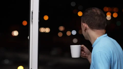 A man drinks hot tea and looks at the lights of the night city Stock Footage 130383353