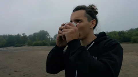 A man drinks hot tea at dawn on the beach Stock Footage 115988341