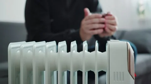 A man drinks hot tea in front of an electric heater at home. The concept of Stock Footage 254060619
