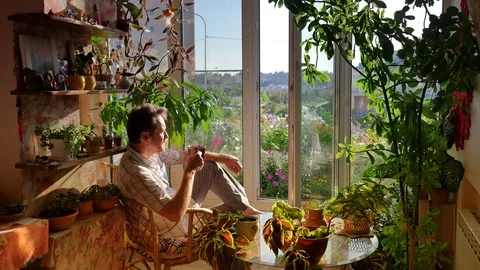 Man Drinks Hot Tea Looking Through Open Window Terrace Decorated With a Lot of 動画素材 71647105