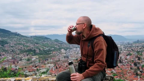 Man drinks hot tea sitting on the mountain top with an old european city view. Stock Footage 246632721