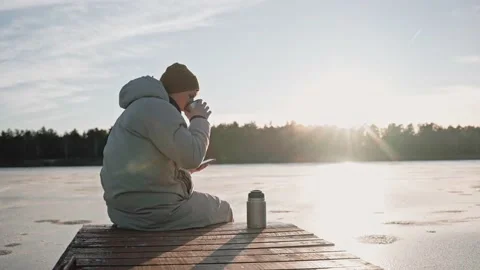 Man drinks hot tea from thermos sitting on a lake dock on a sunny winter day Stock-Footage 170161572