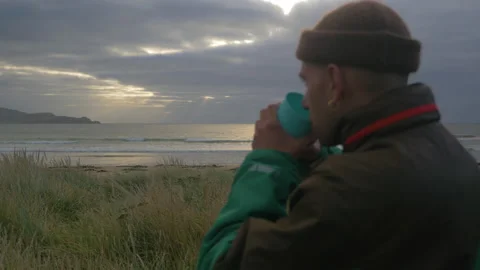 A man drinks hot tea while watching the ocean at sunrise, in New Zealand Stock Footage 219238214