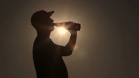 A man drinks from a plastic bottle. Silhouettes at sunset. Stock Footage 105197876