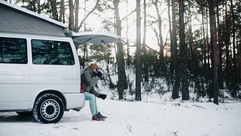 Man drinks sitting in the back of a van with pop up roof in the woods in winter 스톡 동영상 169502380