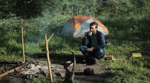A man drinks tea and clicks on the phone near a fire. Against the background is Video stock 64311076